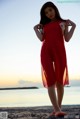 A woman in a red dress standing on a beach.